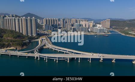 Vue aérienne du pont Cross Bay Link enjambant l'eau bleue avec des immeubles résidentiels de grande hauteur et des montagnes sous un ciel clair New Territori Banque D'Images