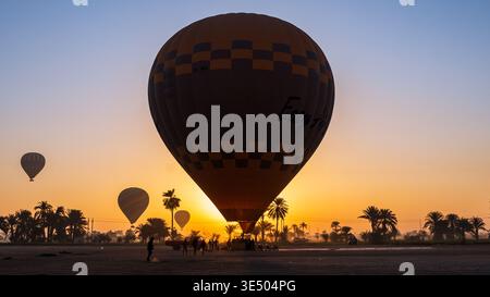 Grande montgolfière à damiers étiquetée « Easy Air » au sol, équipage se préparant au lancement, autres ballons levant, Louxor, Egypte Banque D'Images