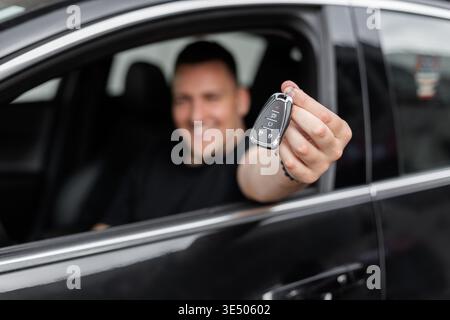 Heureux homme beau assis dans la voiture et tenant les clés. Louez une voiture. Achat de transport Banque D'Images