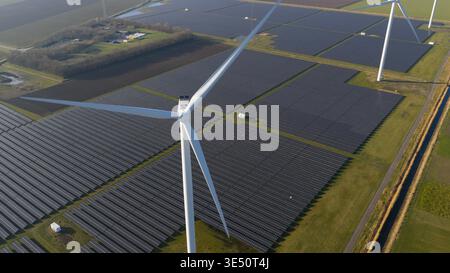 Vue aérienne d'une vaste ferme solaire et d'éoliennes générant de l'énergie propre à travers des champs verts sous un ciel dégagé. Banque D'Images