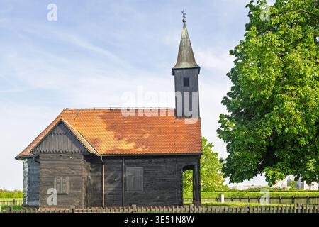 Une chapelle en bois historique pittoresque avec un toit de tuiles rouges sous un ciel serein, entouré de champs verdoyants et d'une nature florissante, exsudant la tranquillité a Banque D'Images
