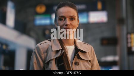 Jeune femme élégante et professionnelle se tient en toute confiance dans le hall des départs de l'aéroport. Émotions positives de voyage, anticipation des vacances et style de vie insouciant de la femme indépendante moderne. Portrait. Banque D'Images