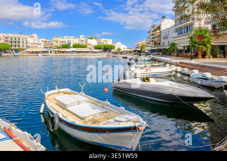 Bateaux de pêche le long du front de mer avec des cafés de trottoir à l'arrière sur le lac Voulismeni dans la ville balnéaire pittoresque d'Agios Nikolaos, Grèce, île de Crète Banque D'Images