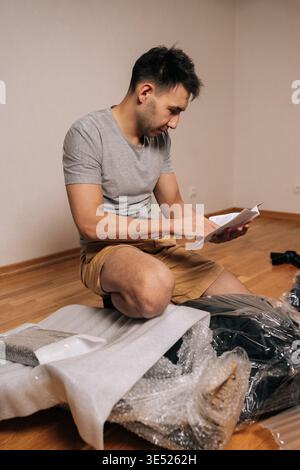 Portrait vertical de l'homme concentré lisant les instructions de montage pour la nouvelle chaise de bureau, déballage des meubles des boîtes, travail sur le projet de bricolage Banque D'Images