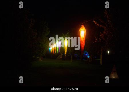 Scène nocturne en plein air avec une chaîne de grandes lanternes illuminées en tissu suspendues sur une ligne entre les arbres. Les lanternes brillent en éclat Banque D'Images