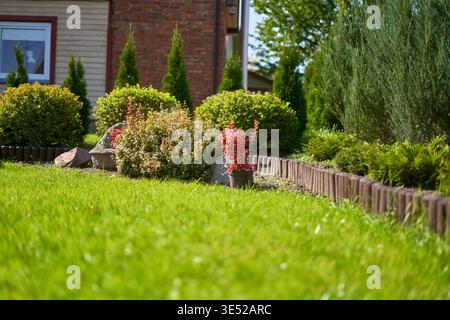 Un jardin résidentiel magnifiquement entretenu avec pelouse verte luxuriante au premier plan et lits de jardin paysagers bordés de bordures en bois. Le Banque D'Images