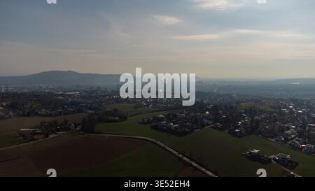 Vue aérienne de Linz, Autriche, une ville européenne tentaculaire nichée entre des champs verdoyants et des montagnes brumeuses lointaines, avec des cheminées industrielles Banque D'Images