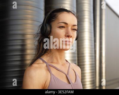 Portrait détaillé d'une jeune femme portant un casque sans fil debout à l'extérieur au coucher du soleil Banque D'Images