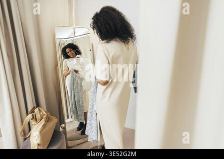 Jeune femme élégante dans les cabines d'essayage regardant le miroir essayer de nouveaux vêtements Banque D'Images