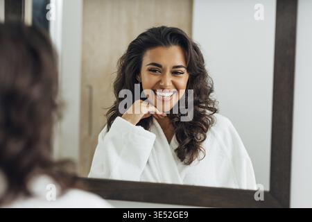 Reflet de la femme heureuse dans le miroir portant un peignoir blanc Banque D'Images