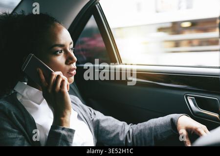 Young businesswoman talking on mobile phone, assis sur le siège arrière d'une voiture Banque D'Images