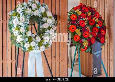 Deux couronnes funéraires détaillées sur des stands. A gauche : roses rose pâle et verdure. Droite : gerberas orange rouge vif et alstroemeria jaune avec une main Banque D'Images