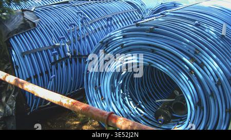 Gros plan de grandes bobines de tuyaux en plastique bleu, éventuellement pour l'irrigation ou la construction, avec un tuyau en métal rouillé au premier plan Banque D'Images
