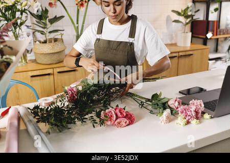 Fleuriste femme faisant un bouquet au comptoir dans un petit magasin de fleurs Banque D'Images