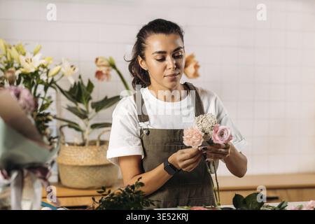 Femme debout à table faisant un bouquet de fleurs fraîches. Fleuriste féminine travaillant dans un magasin de fleurs Banque D'Images
