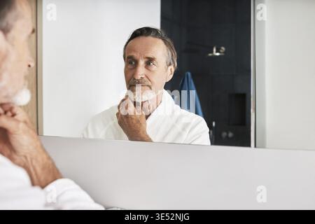 Beau homme en peignoir inspectant sa peau Banque D'Images