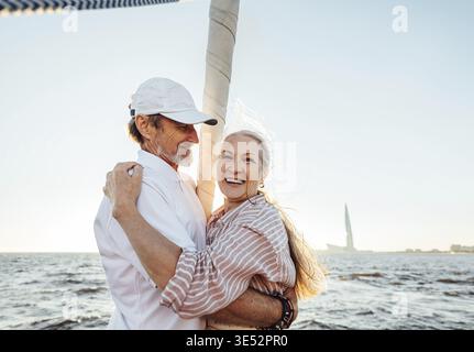 Joyeux couple mûr embrassant à l'extérieur. Heureuse femme senior regardant la caméra tout en se tenant sur l'arc de yacht avec son mari Banque D'Images
