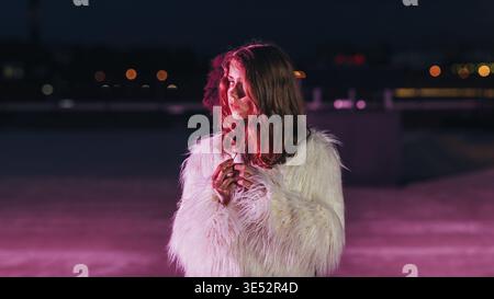 Jeune femme blonde debout sur un toit devant une lumière rose fluo et regarder loin Banque D'Images