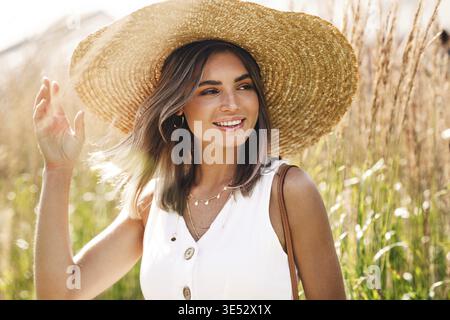 Jeune femme heureuse portant un gros chapeau de paille debout sur le terrain Banque D'Images
