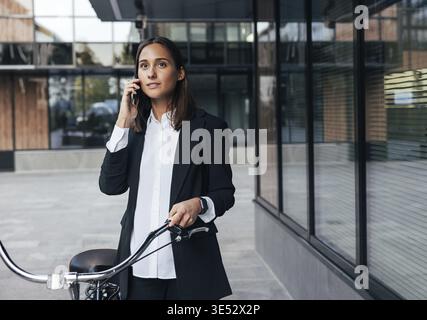 Jeune femme élégante dans des vêtements formels noirs avec vélo Banque D'Images
