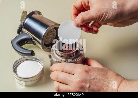 Une personne prépare un pot de moka pour l'infusion en ajoutant un filtre en papier, assurant une expérience de café plus propre et plus riche Banque D'Images