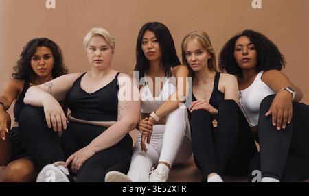 Cinq femmes différentes dans les vêtements de sport assis ensemble et regardant la caméra Banque D'Images