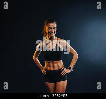 Portrait d'une jeune femme musclée gaie dans des vêtements de sport posant sur fond noir Banque D'Images