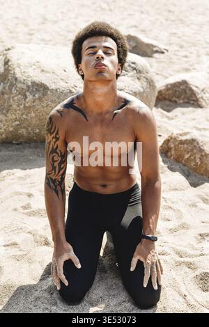 Assez musclé homme assis sur le sable, avec la tête et les yeux fermés Banque D'Images