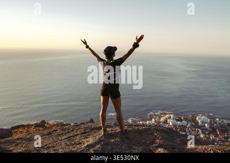 Vue arrière de la femme en forme debout sur le sommet de la montagne en regardant la vue avec les bras larges ouverts Banque D'Images