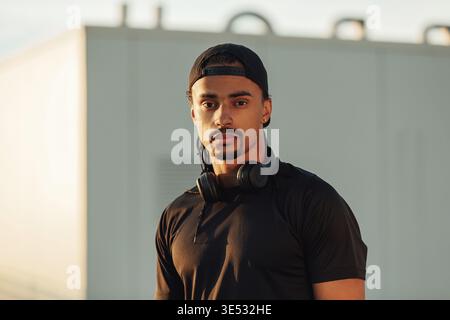 Portrait d'un athlète masculin confiant portant une casquette noire, un casque sans fil et des vêtements de sport regardant l'appareil photo Banque D'Images