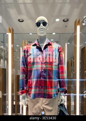 Un mannequin se tient dans une vitrine pour exposer des vêtements et des lunettes de soleil. Banque D'Images