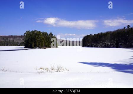 Une vaste étendue enneigée de lac Philippe gelé est encadrée par des collines densément boisées sous un ciel bleu vif dans le parc de la Gatineau, au Québec Banque D'Images