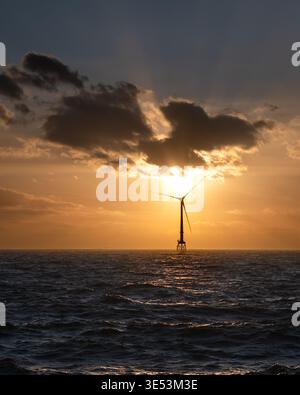 Des éoliennes offshore se sont dessinées contre un coucher de soleil ambré flamboyant sur la mer du Nord, des rayons crépusculaires traversant les nuages derrière l'éolienne. Banque D'Images