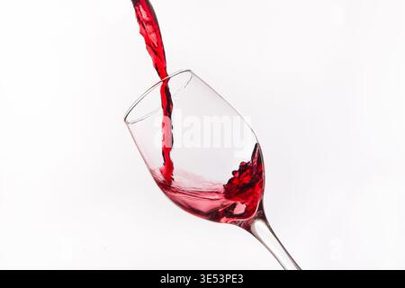 Le vin rouge éclabousse et tourbillonne tout en versant dans un verre transparent Banque D'Images