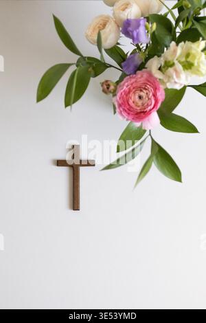 Composition minimale avec croix en bois et fleurs de printemps fraîches sur fond blanc. Christianisme, foi, prière, Pâques et concept de dévotion spirituelle Banque D'Images