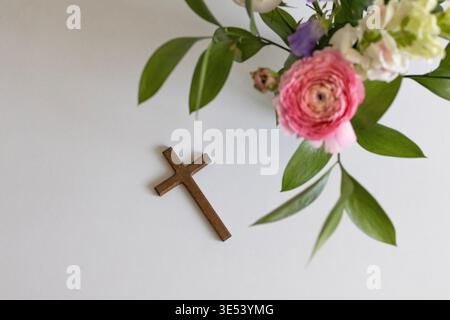 Composition minimale avec croix en bois et fleurs de printemps fraîches sur fond blanc. Christianisme, foi, prière, Pâques et concept de dévotion spirituelle Banque D'Images