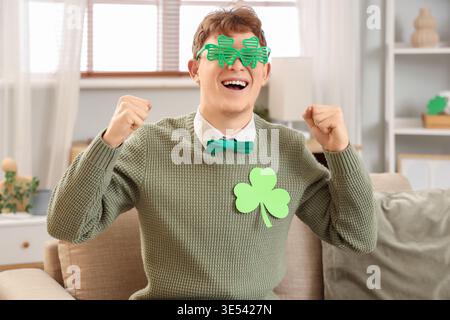 Jeune homme roux en lunettes avec trèfle assis à la maison le jour de Patrick Banque D'Images