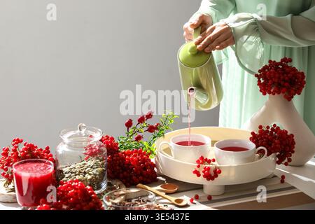 Jeune femme versant du thé viburnum de la théière dans la tasse à la maison Banque D'Images
