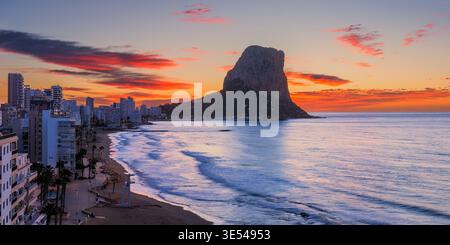Une large photographie panoramique 2 :1 du lever du soleil prise depuis une position légèrement surélevée le long de la plage de Calpe (Calp), en regardant vers l’emblématique Peñón de If Banque D'Images
