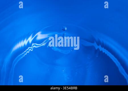 Une goutte d'eau tombe et rebondit sur une surface humide sur un fond bleu Banque D'Images