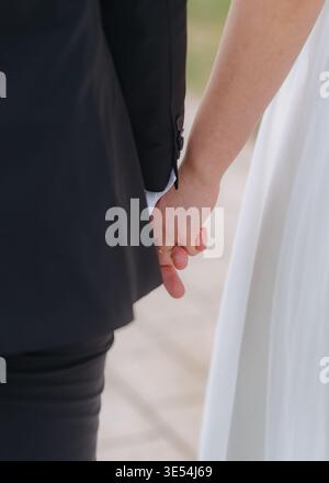 Gros plan de mariés se tenant par la main. Symbole d'amour, de confiance et d'engagement. Moment de mariage émotionnel avec lumière naturelle douce. Banque D'Images
