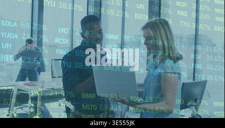 Parlant homme et femme collègues tenant un ordinateur portable dans le bureau portant des affaires décontractées, superposition de stock Banque D'Images