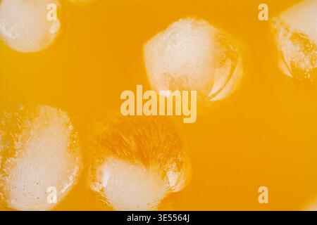 Gros plan jus d'orange avec glace, scène de petit déjeuner ensoleillée montrant des cubes flottants, lueur chaude, gouttelettes de condensation minuscules, tonus de vitamine C revigorant, brea Banque D'Images