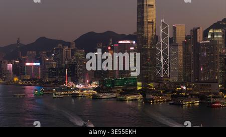Hong Kong - 13 février 2026 : vue aérienne de la ville illuminée de Hong Kong la nuit avec le port Victoria, les ferries et la tour Bank of China. Banque D'Images