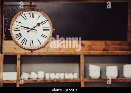 Horloge de station vintage double face suspendue dans un intérieur de café rustique. Le design classique avec des chiffres romains est entouré d'étagères en bois et de guerre Banque D'Images