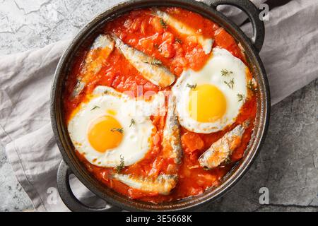 Délicieux œufs frits avec des sardines dans une sauce tomate de légumes gros plan dans une poêle sur la table. Vue horizontale de dessus Banque D'Images
