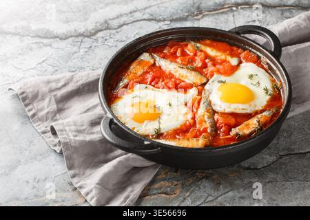 Œufs frits maison avec sardines dans une sauce tomate épicée gros plan dans une poêle sur la table. Horizontal Banque D'Images