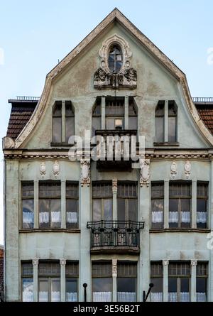 Façade avant d'une ancienne maison de ville historique avec pignon orné, grandes fenêtres, balcons et stuc altéré, tourné directement sur le ciel bleu. Banque D'Images