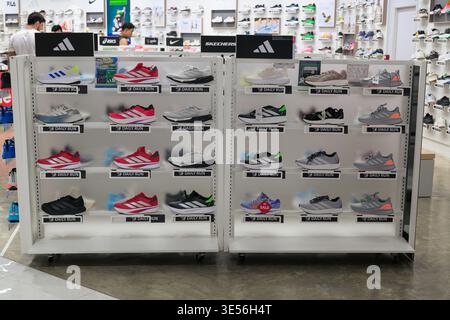 Une vue intérieure grand angle d'une section de vêtements de sport très éclairée avec des rangées de chaussures de sport sur des étagères blanches. L'arrière-plan montre shoppers A. Banque D'Images