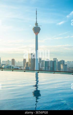 Ligne d'horizon de Kuala Lumpur avec tour s'élevant au-dessus des bâtiments de la ville reflétée dans la piscine à débordement sur le toit au lever du soleil, Malaisie. Développement urbain Banque D'Images